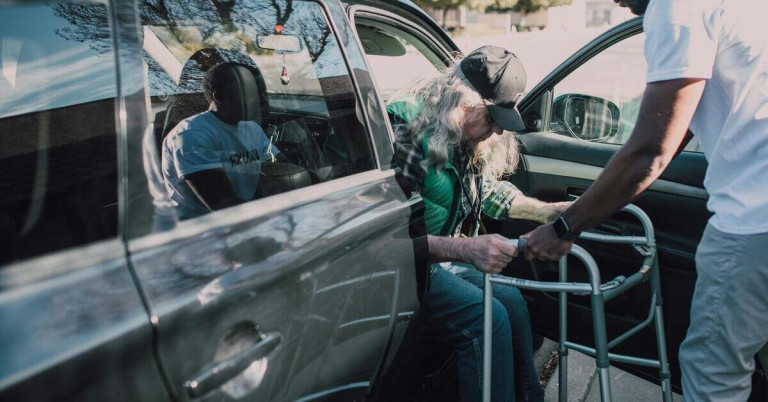 Älterer Mann steigt mit Hilfe eines Gehgestells aus einem Auto aus