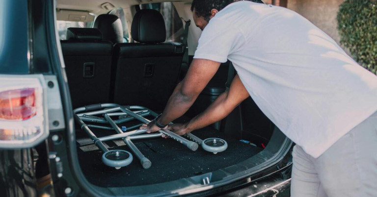 Mann zerlegt Gehhilfe und verstaut sie im Kofferraum eines Autos