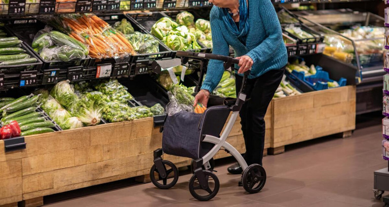 Ältere Frau mit Rollator beim Einkaufen von frischem Gemüse im Supermarkt
