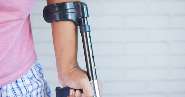 Unterarm mit Krücke vor heller Wand