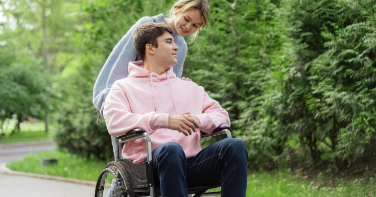 Junger Mann im Rollstuhl mit Begleitperson im Park