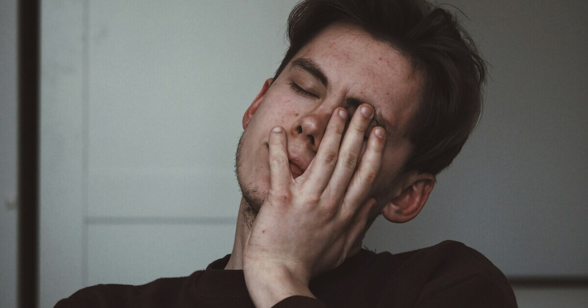 Junger Mann wirkt müde und antriebslos, sitzt nachdenklich vor hellem Hintergrund