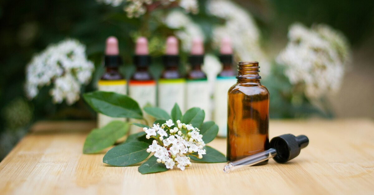 Braunes Fläschchen mit Pipette, Blüten und Bachblüten-Essenzen im Hintergrund