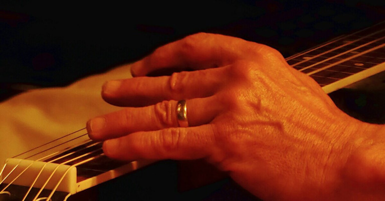 Nahaufnahme einer Hand mit belastetem Nagel auf einer Gitarrensaite