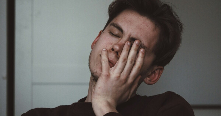 Müdigkeit Symbolbild: Person hält sich den Nacken und wirkt erschöpft