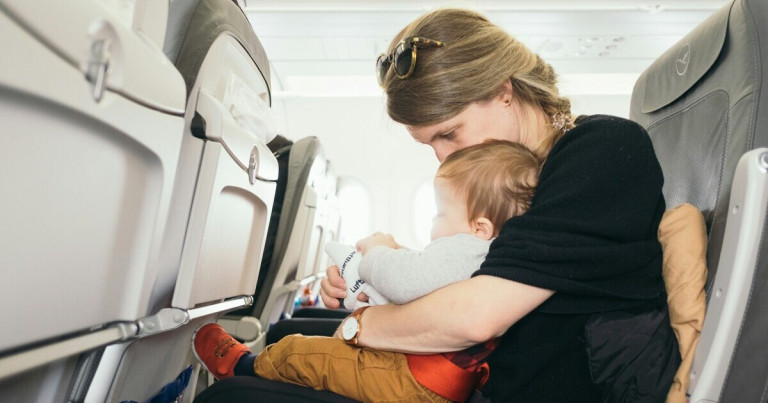 Baby im Flugzeug – Tipps für das Fliegen mit Kleinkindern Baby im Flugzeug auf dem Schoß einer erwachsenen Person während des Fluges