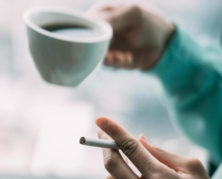 Rauchen kann Schweißgeruch verschlechtern – Hand mit Zigarette und Kaffeetasse