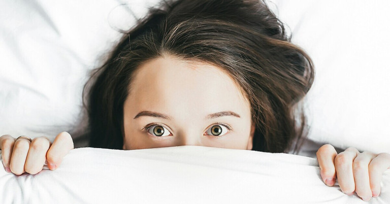 Pavor nocturnus: Frau mit braunen Haaren liegt im Bett und erlebt einen Nachtschreck