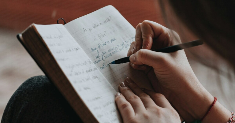 Person schreibt in ein Tagebuch mit einem Stift auf einer aufgeschlagenen Seite