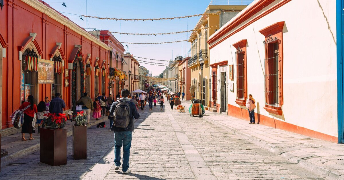 Belebte Straßenszene in Mexiko mit bunten Häusern und Passanten bei Sonnenschein