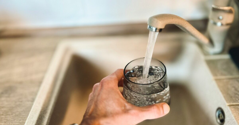 Wasser trinken – Hand hält ein Glas unter einen Wasserhahn und füllt es mit frischem Leitungswasser