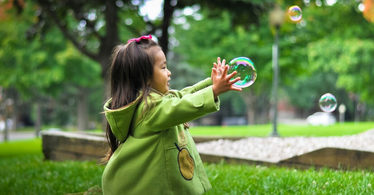 Kind spielt draußen im Park und fängt eine Seifenblase