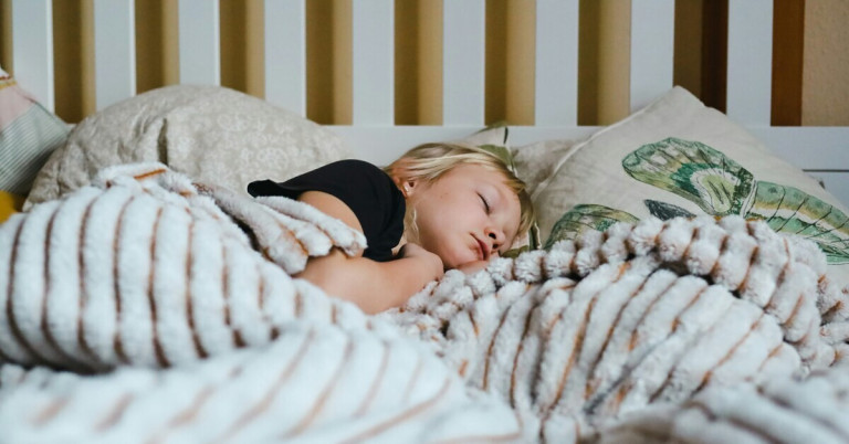 Kind schläft im Bett unter einer Decke