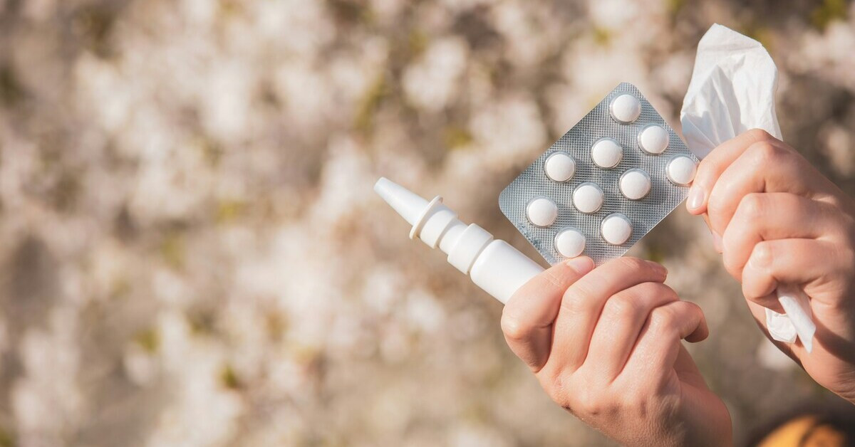 Hand hält Medikamente und Taschentuch, Nasenspray und Tabletten gegen Erkältung oder Allergie