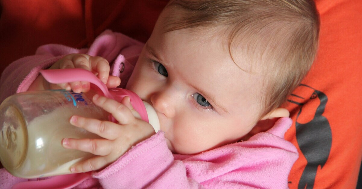 Baby trinkt aus einer Flasche in rosa Kleidung