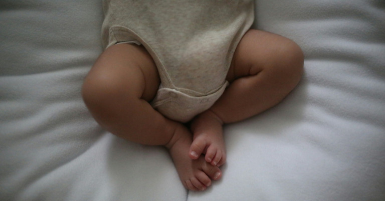 Baby in dünnem Body auf weißer Decke