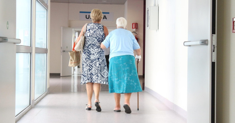 Zwei Seniorinnen gehen gemeinsam durch den Flur einer Praxis