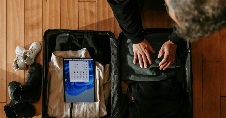 Koffer packen mit Kleidung und Tablet auf Holzfußboden