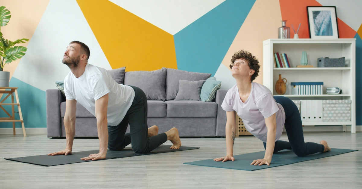 Yoga gegen Verspannungen in Schulter und Nacken – zwei Personen machen Yoga-Übungen im Wohnzimmer