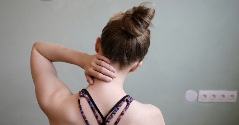 Frau mit Verspannungen im Nacken und Schulter, Hand am Nacken