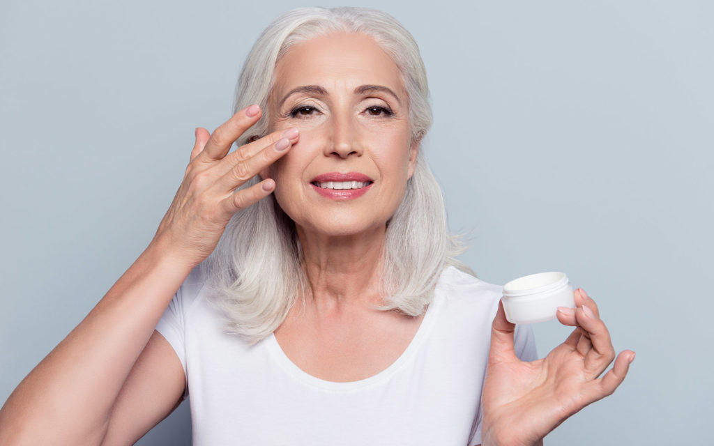 Ältere Frau trägt Kosmetikcreme auf ihr Gesicht auf