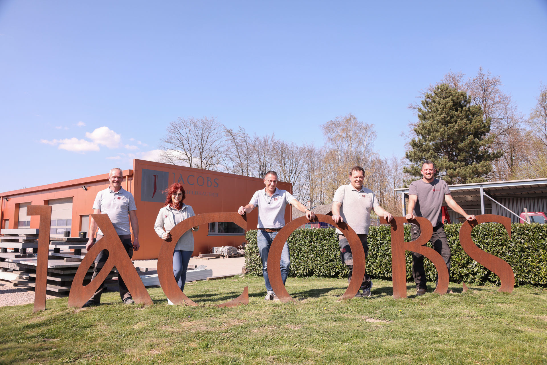 Team der Firma Jacobs Metallbauerei vor dem Firmengebäude mit großen Metallbuchstaben