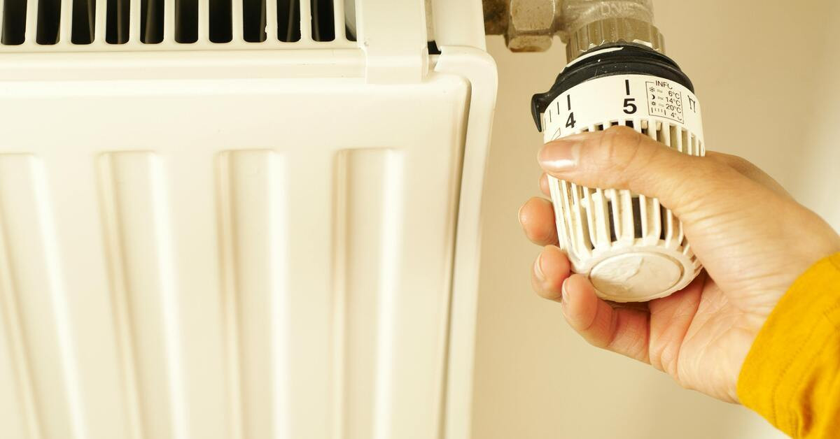 Hand dreht an Thermostat eines Heizkörpers zur Temperaturregelung