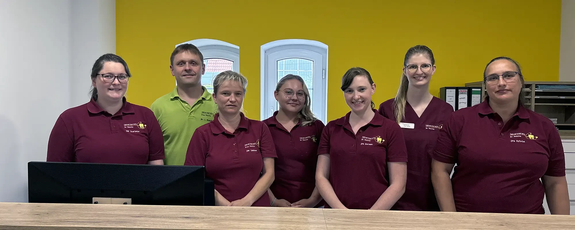 Gruppenbild eines Praxisteams vor gelber Wand