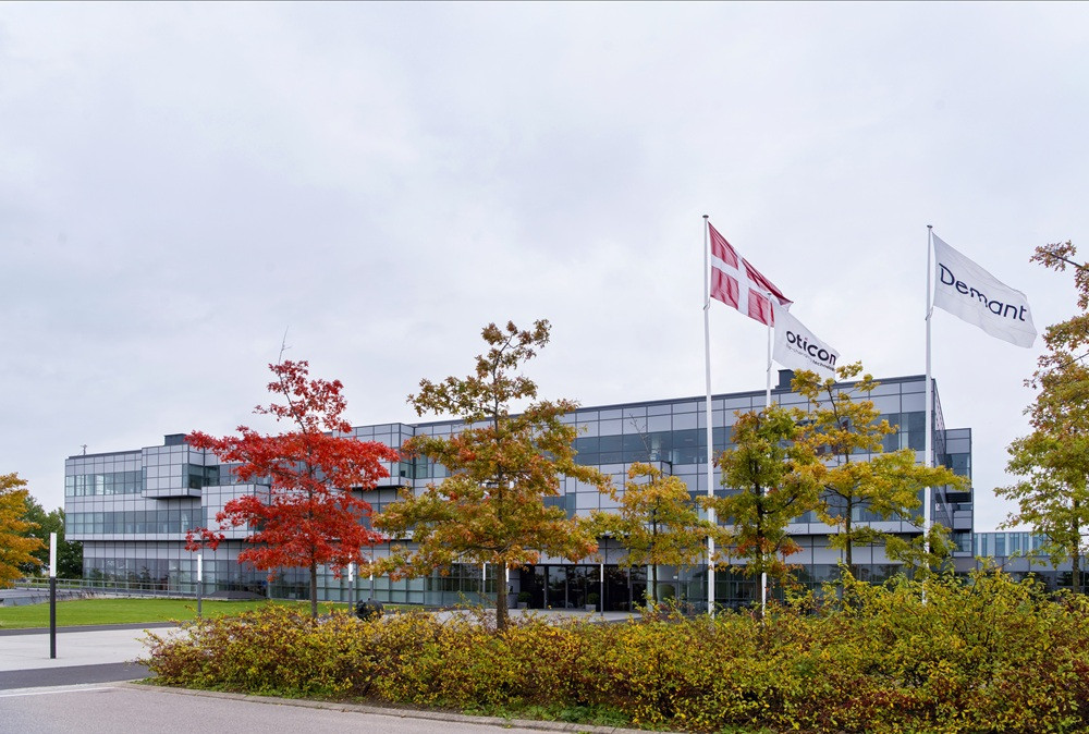 Demant Zentrale mit dänischer Flagge und Oticon-Logo Demant Zentrale mit dänischer Flagge und Oticon-Logo