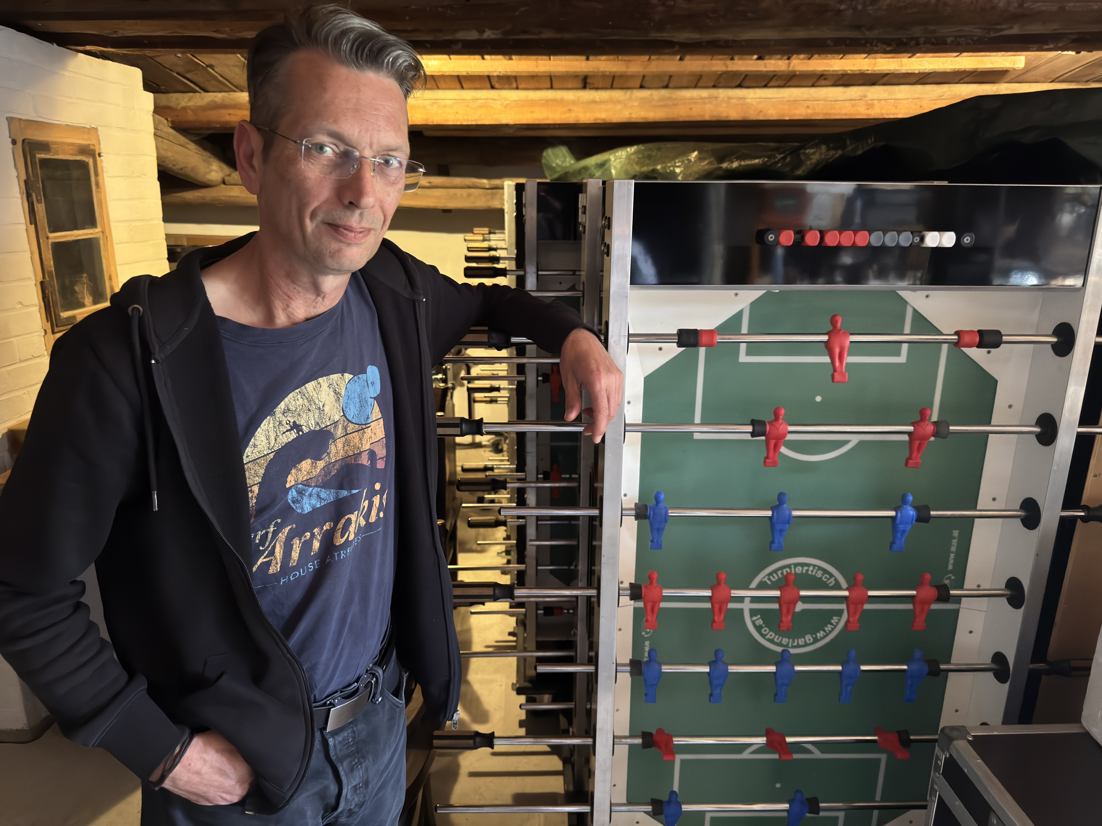 Mann neben Kickertisch in rustikalem Raum Mann steht neben einem Kickertisch in einem Raum mit Holzbalken