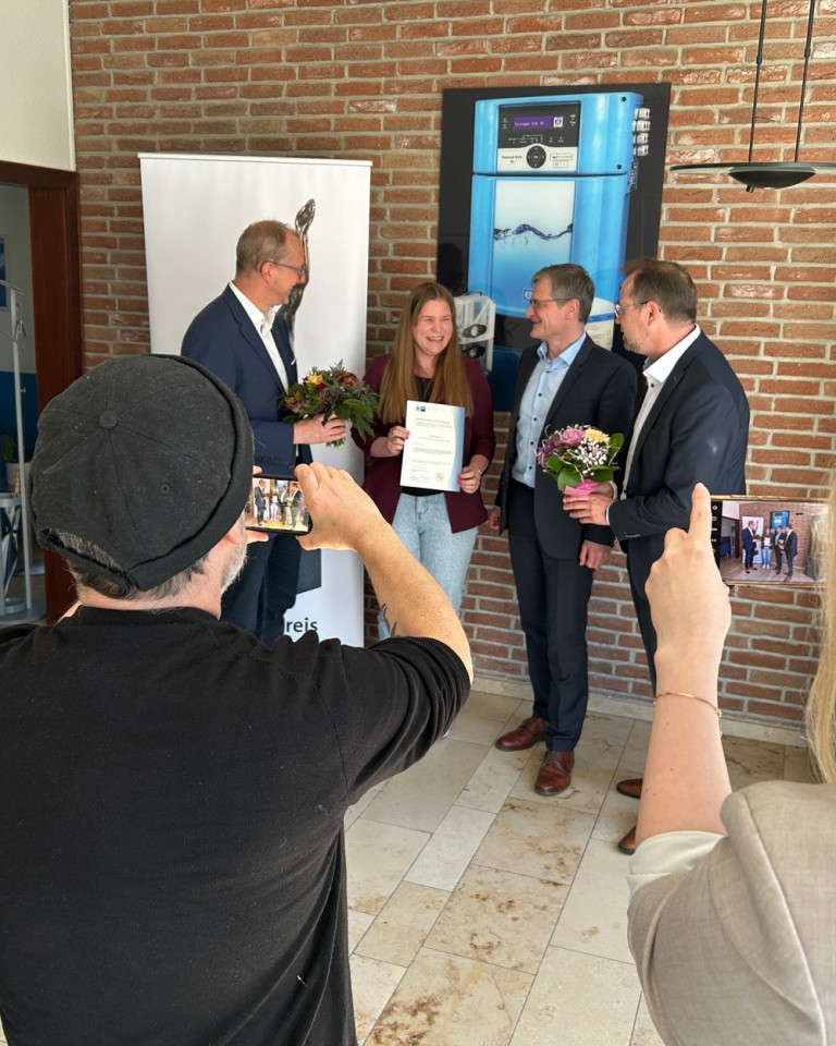 Anerkennungsübergabe – Offizielle Übergabe einer Urkunde mit Blumen Anerkennungsübergabe mit mehreren Personen, Blumen und Urkunde in einem offiziellen Rahmen