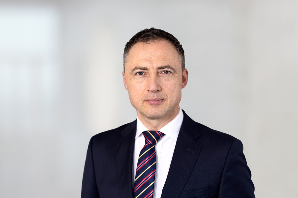Mirko Hoppe im Anzug mit gestreifter Krawatte vor neutralem Hintergrund