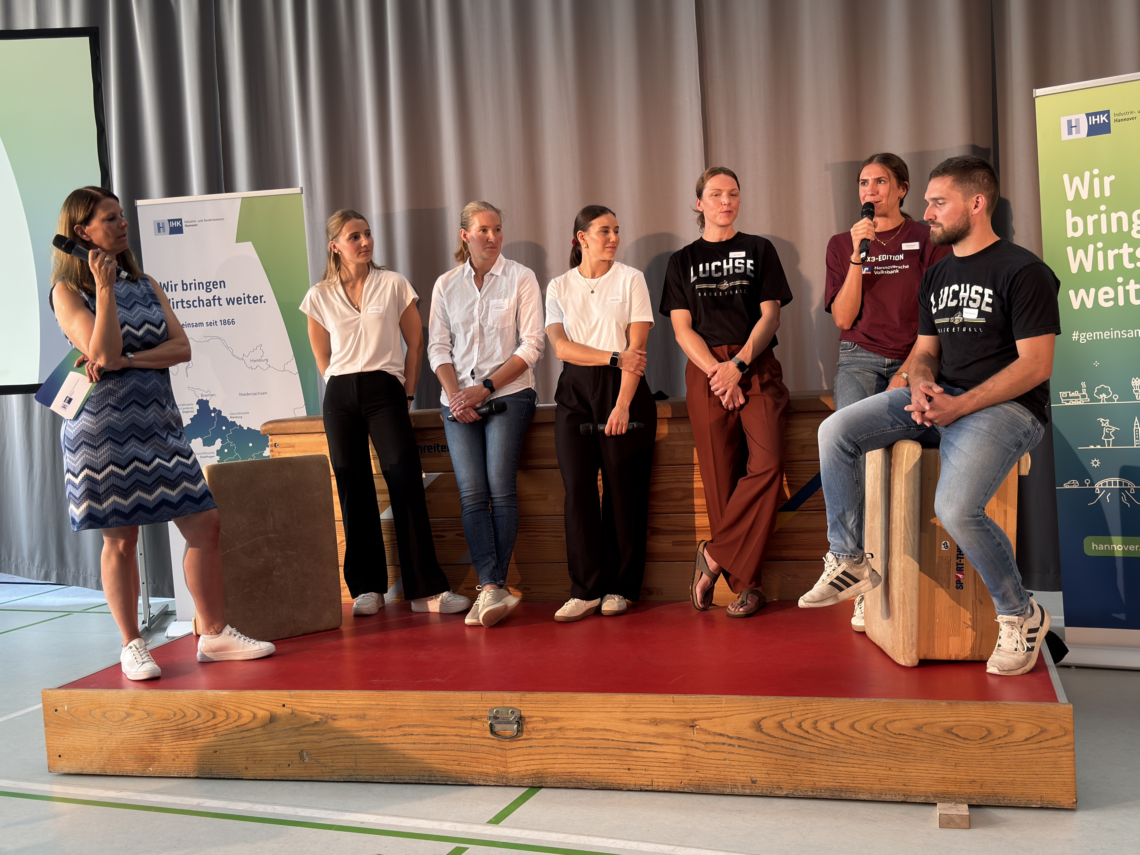 Podiumsdiskussion mit jungen Erwachsenen auf einer Bühne, IHK Banner im Hintergrund, Teilnehmer tragen Luchse T-Shirts