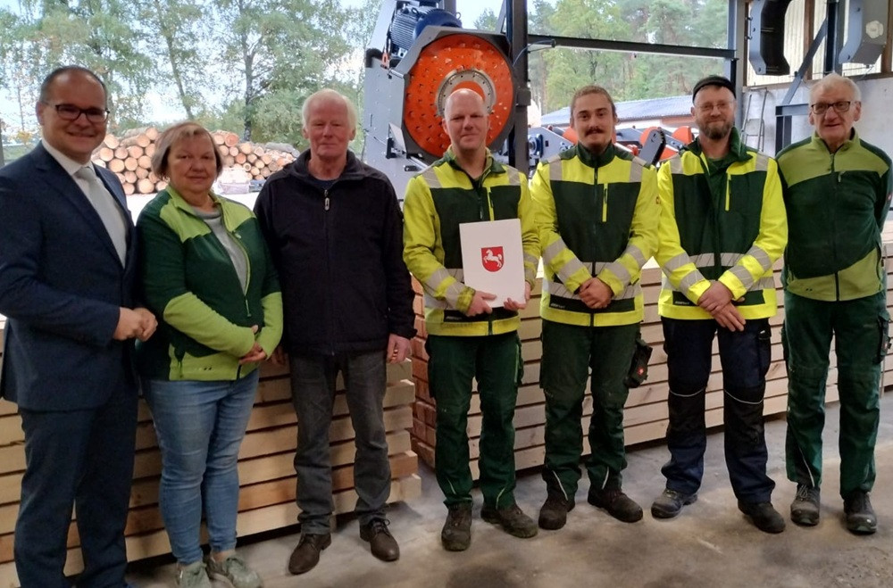 Gruppenfoto bei Lichtsinn – Mitarbeiter vor Holzstapeln und Maschinen Gruppenfoto bei Lichtsinn mit mehreren Personen in Arbeitskleidung vor Holzstapeln und Maschinen
