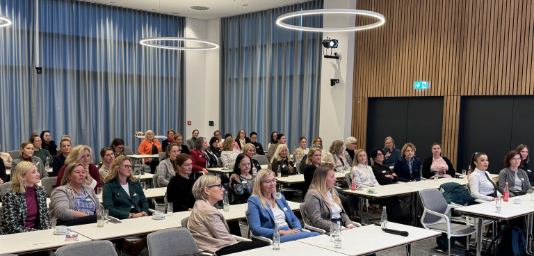 Teilnehmer einer Konferenz oder Tagung in einem modernen Konferenzraum mit großen Fenstern und runden Deckenleuchten