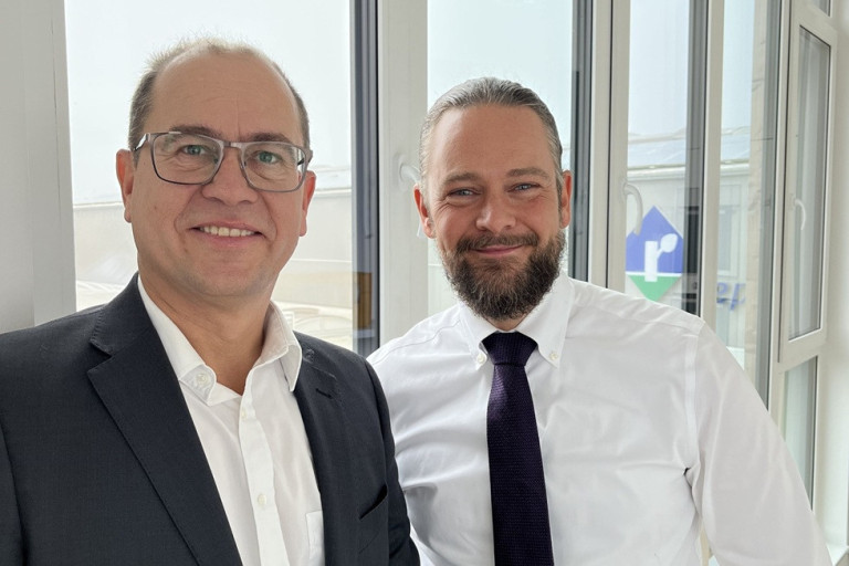 Bradtmoller und Goos geschäftlich gekleidet vor moderner Fensterfront Bradtmoller und Goos im Business-Outfit vor Fenstern