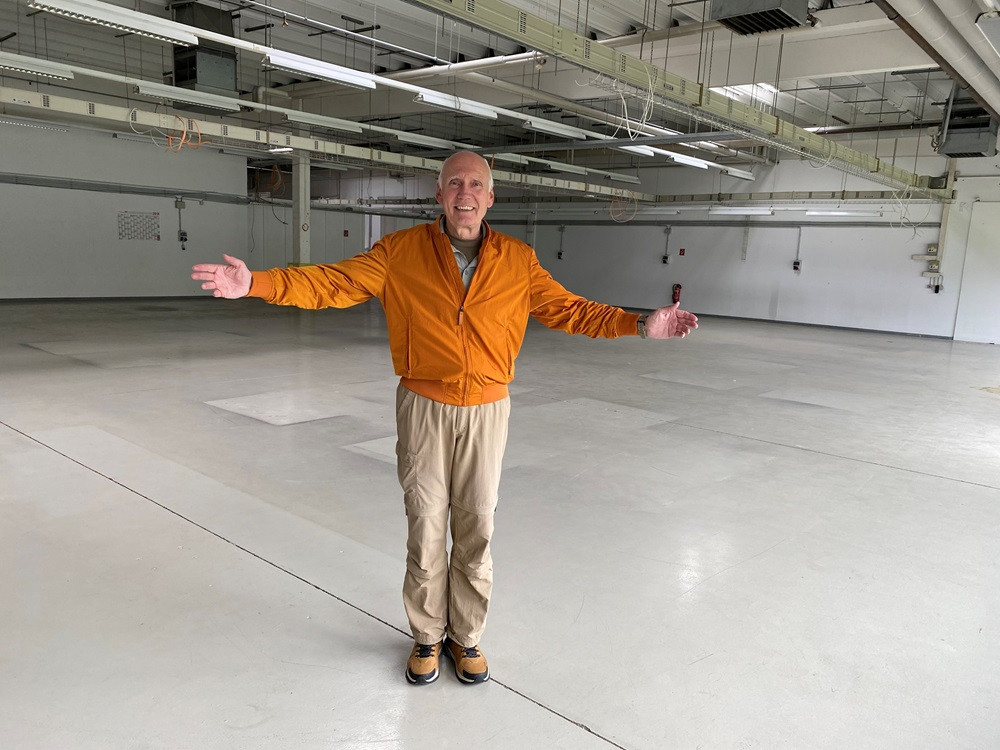 Uwe Lampe steht mit ausgebreiteten Armen in einer großen, leeren Halle.