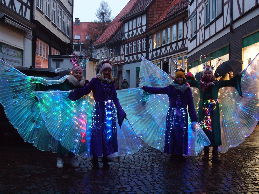 Kostümierte Personen mit leuchtenden Flügeln bei einem Lichterfest in einer Altstadt mit Fachwerkhäusern