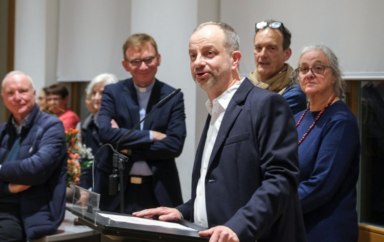 Ausstellungsmacher spricht auf Vernissage – Gruppenfoto am Rednerpult Ausstellungsmacher bei einer Rede auf einer Vernissage, mehrere Personen stehen am Rednerpult