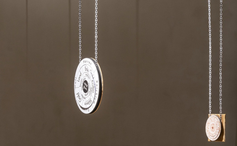 Spulen-Anhänger als Schmuckstück – modernes Design mit Gravur Design-Anhänger in Spulenform mit Gravur, an einer Kette hängend vor braunem Hintergrund