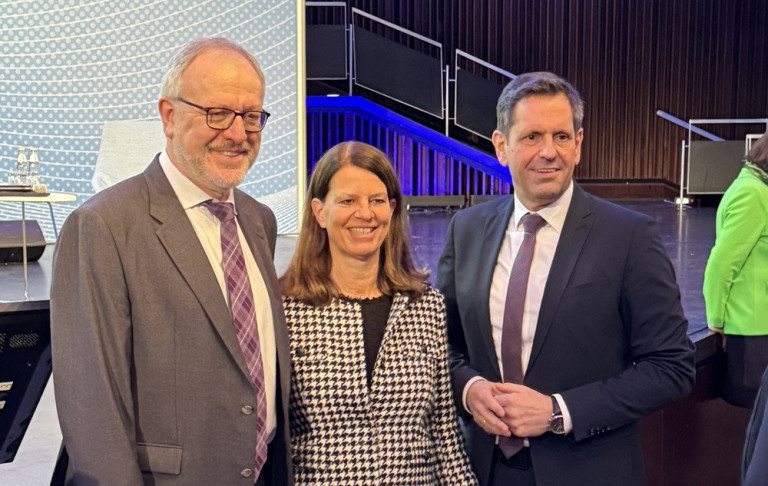 Gruppenfoto beim Auftakt-Event auf einer Bühne mit mehreren Personen im Business-Outfit