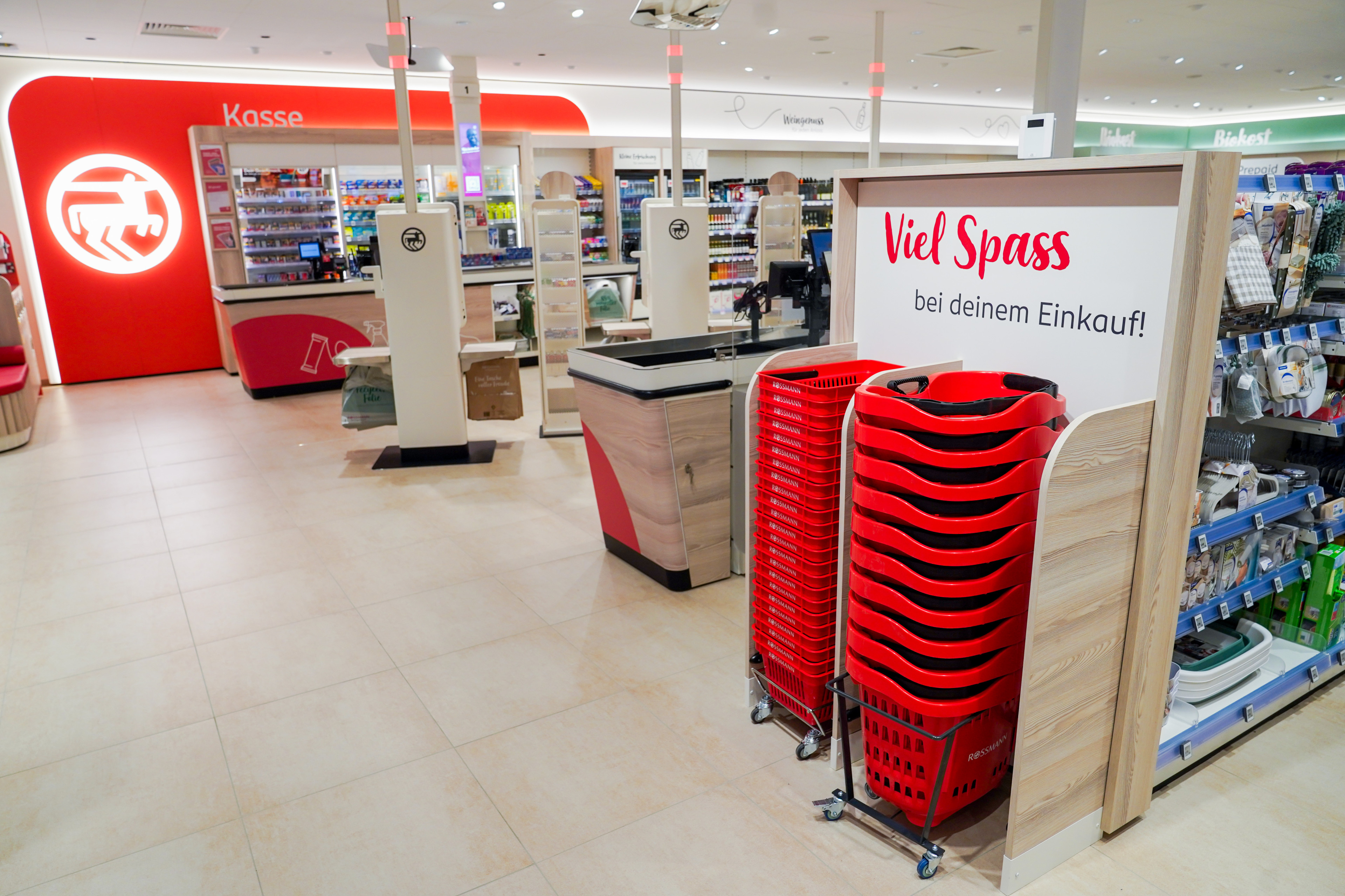 Moderner Eingangs- und Kassenbereich in einem Drogeriemarkt mit roten Einkaufskörben und freundlicher Begrüßung