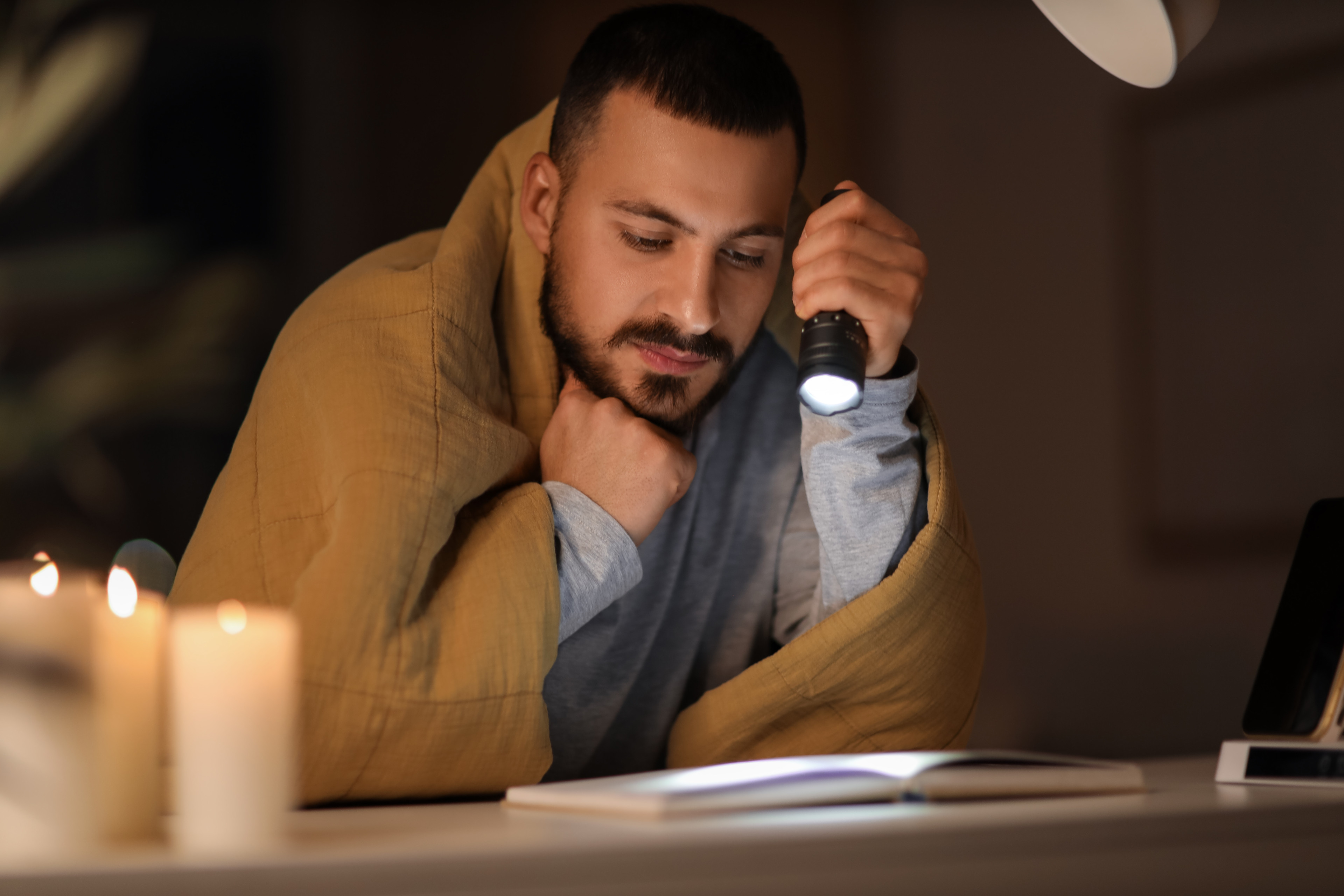 Person liest nachts unter einer Decke mit Taschenlampe und Kerze