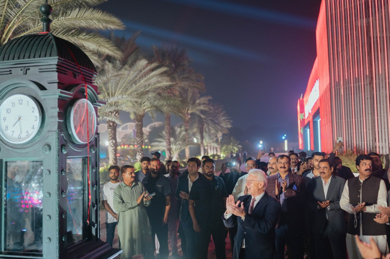 Menschenmenge bei Nachtveranstaltung mit Palmen in Lahore, neben einer großen Uhr und beleuchteten Gebäuden