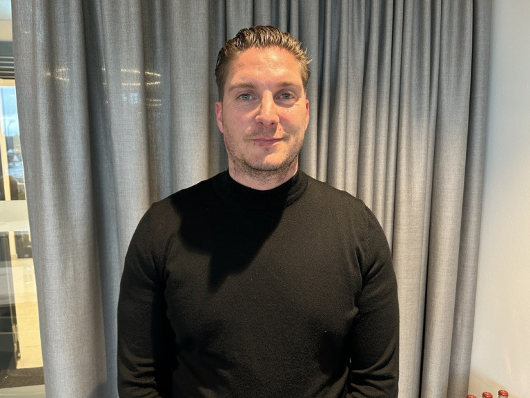 Nicolas Schweinert vor grauem Vorhang in schwarzem Pullover