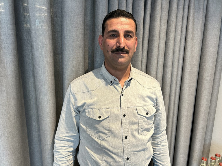 Allan Abdulla in einem hellen Hemd vor einem grauen Vorhang