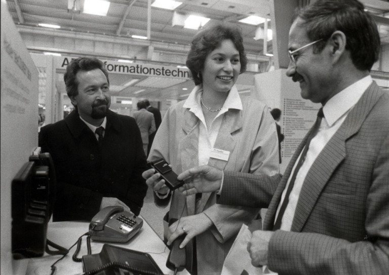 Historisches Foto vom CeBIT-Stand: Menschen präsentieren frühe Informationstechnologie und Telefone