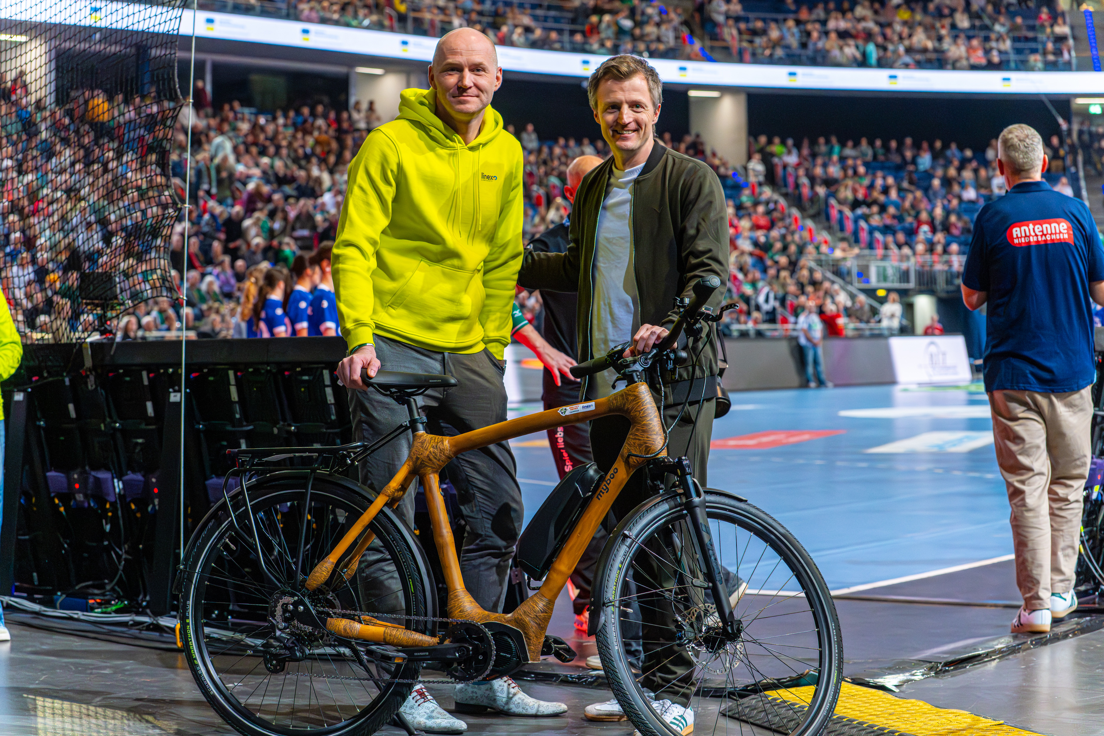 Zwei Personen mit einem Bambusfahrrad bei TSV Hannover gegen HSG Wetzlar Handballspiel in einer vollen Arena
