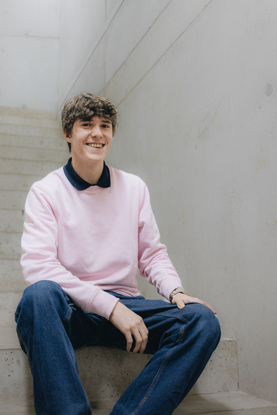 Noah Möhring sitzt auf einer Treppe und trägt einen rosa Pullover