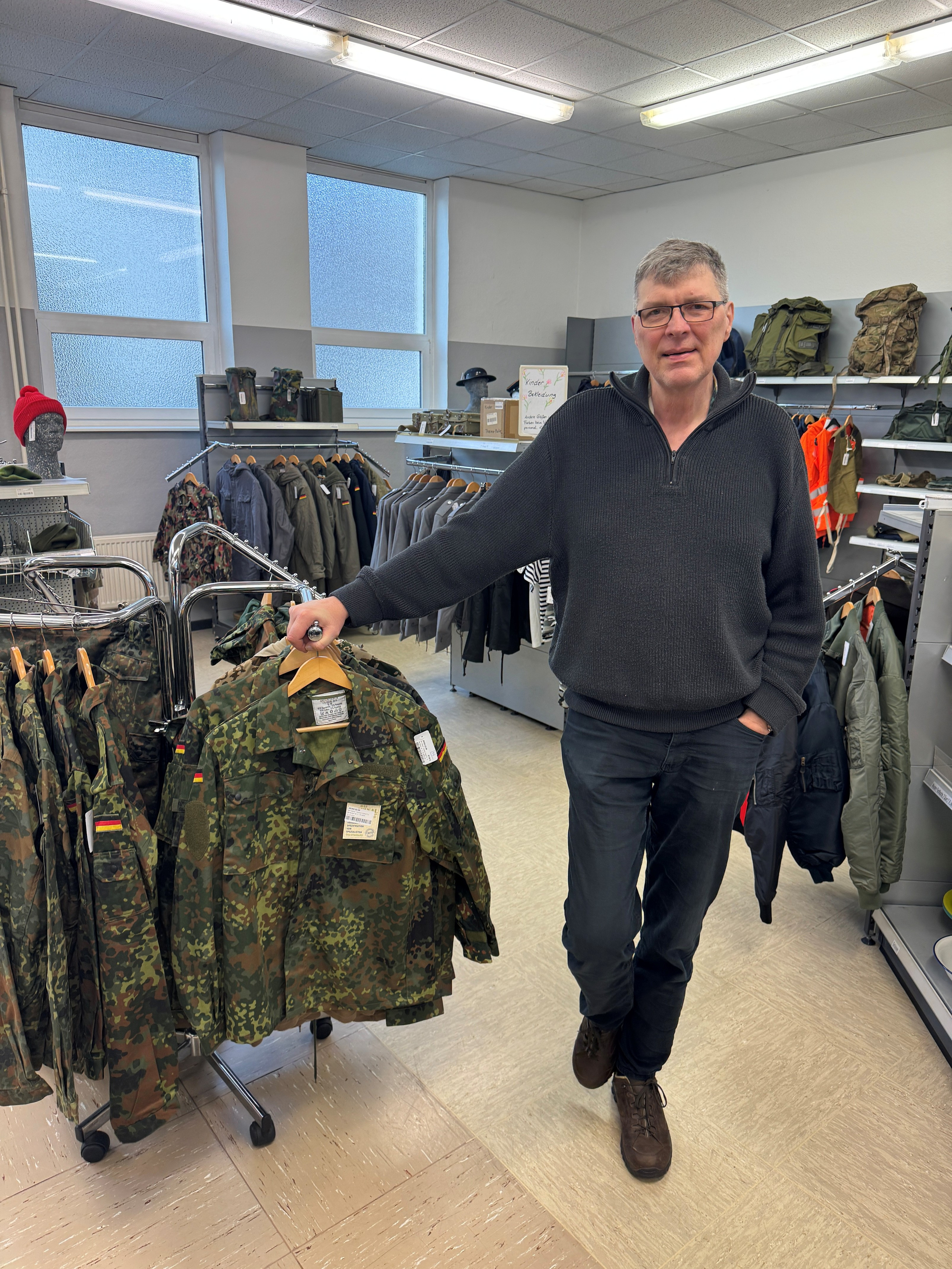 Mann in einem Army-Shop steht neben Bundeswehr-Feldjacken auf Kleiderständern